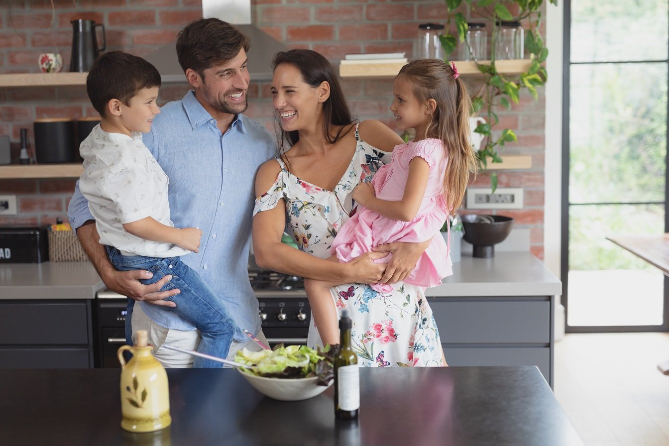 Front view of happy Caucasian family preparing vegetable salad in kitchen at home